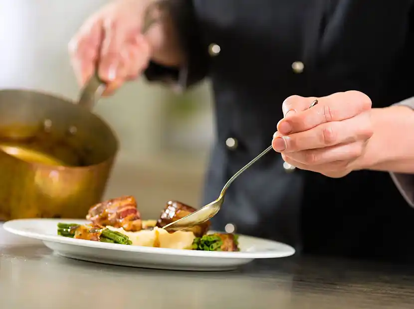 Koch richtet Essen auf Teller an und gibt Sauce dazu.