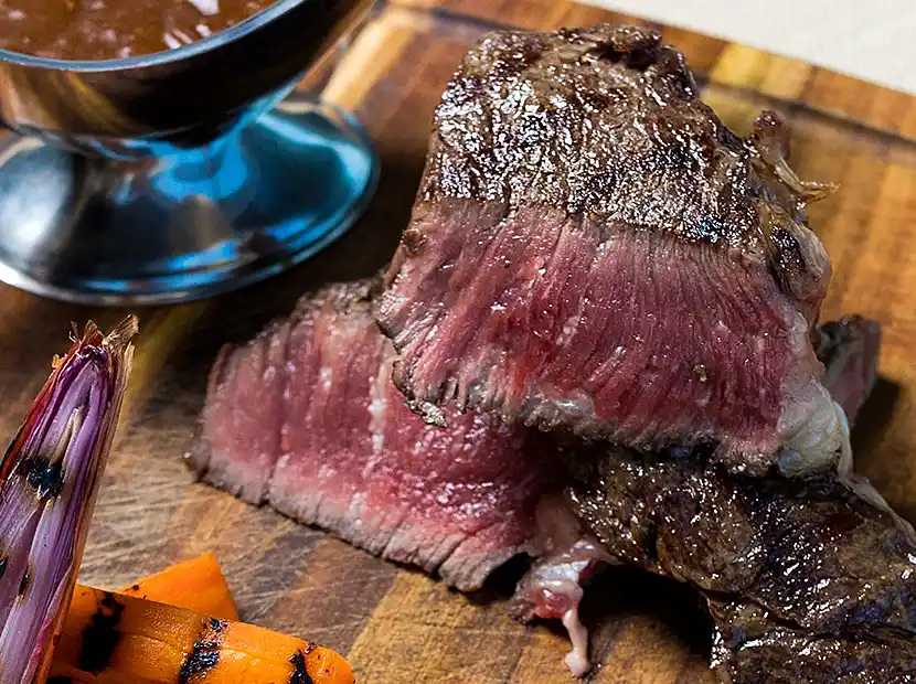 Angeschnittenes, saftiges Filetsteak, medium gebraten auf Holzplatte mit Grillgemüse und Bratensoße im kleiner Kanne..