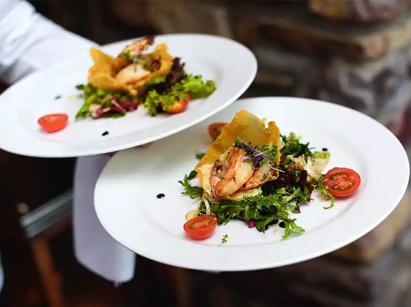 Servierkraft mit 2 Tellern und gebratenen Garnelen auf Salat.