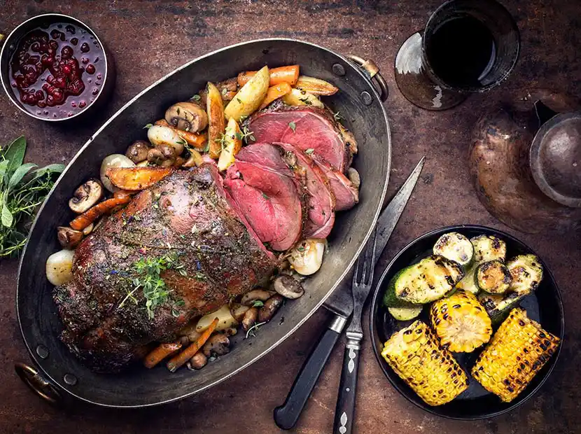 Holztisch mit Bräter gefüllt mit Roastbeef und Bratkartoffeln.