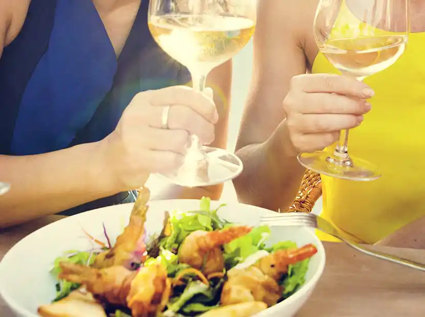 Zwei Frauen mit Weißwein und einer Schale mit gegrillten Garnelen und Salat.