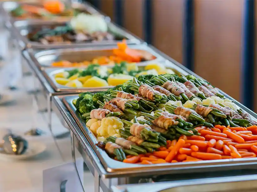 Leckeres Mittagsbuffet wie Bohnen im Speckmantel, Broccoli, Kartoffeln und Karotten in Wärmebehältern angerichtet.