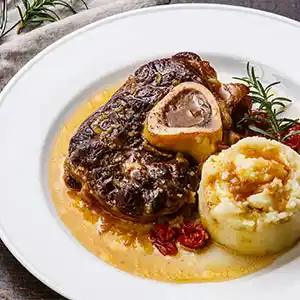 Teller mit Kalbsbeinscheiben und Kartoffelstampf an Bratensauce.