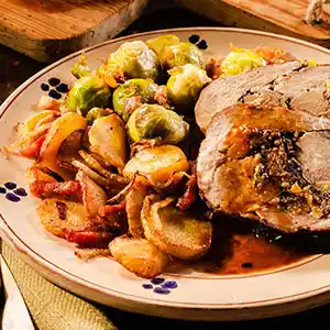 Teller mit Schweinerollbraten, Bratkartoffeln und Rosenkohl an Bratensauce.