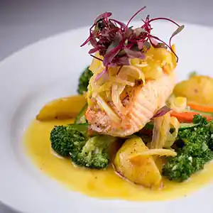 Teller mit Lachsfilet, Gemüse und Kartoffeln an Zitronensauce.