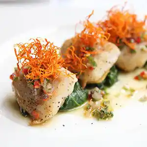 Teller mit Seehecht auf Spinatnestern und Karotten an Buttersauce.