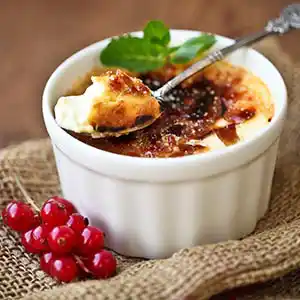 Teller mit Crème brûlée an Johannisbeeren und Minzgarnitur.