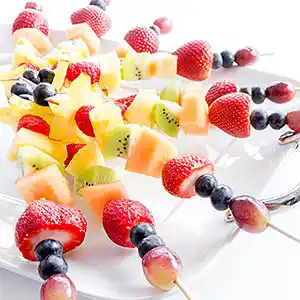 Fruchtspieße mit Beeren, Kiwis, Melonen und Ananas.