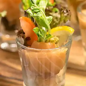 Gebeitzter Lachsröllchen auf Avocado-Kapern-Tartar im Glas.