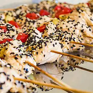 Gebratene Hühnerbruststreifen im Sesammantel an Kirschtomaten am Spieß.