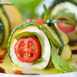 Schälchen mit Mozzarella-Zucchini-Röllchen gefüllt mit Cocktailtomaten und Basilikum.