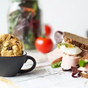 Holzbrett mit Vollkornsandwich, Schinken und Ei, gemischter Salat und Cookie.