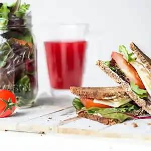 Holzbrett mit Vollkornsandwich, Käse und Tomaten, gemischter Salat und Rharbarbersaft.