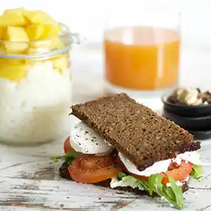 Holzbrett mit Vollkornsandwich, Mozzarella und Tomaten, Nüssen, Orangensaft und Dessert.