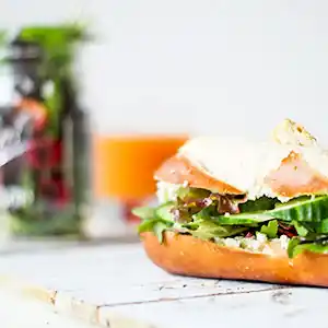 Holzbrett mit Brezenstange, Frischkäse und Gurken, gemischter Salat und Orangensaft.