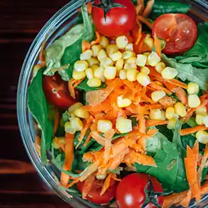 Salatteller mit Spinat, Karotten, Mais und Tomaten.