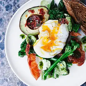 Salatteller mit Broccholi, Avocado, Tomaten, Paprika und pochiertes Ei.
