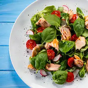 Blattsalatteller mit Kirschtomaten, Radieschen, Lachs und Basilikum.