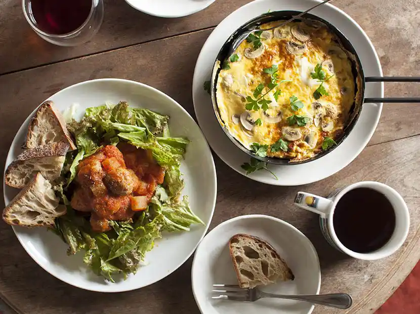 Holztisch mit Rühreiern, Kaffee und Salatteller.
