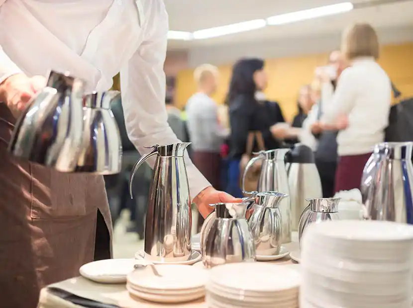 Tisch mit Tellerstapel. Frau bringt Kaffee.