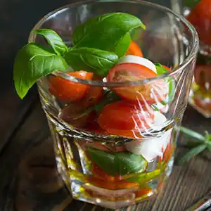 Mozzarella-Kugeln mit Kirschtomaten an Basilikum und Balsamicodressing im Glas.