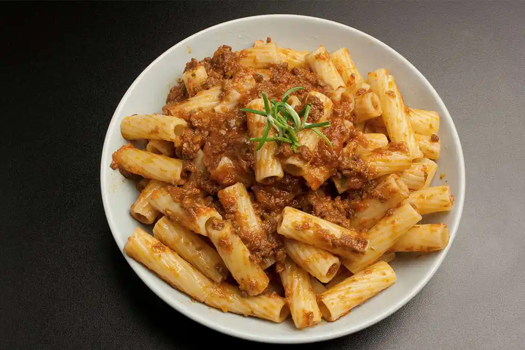 Teller mit Nudeln, Fleischsauce, Tomaten und Karotten.