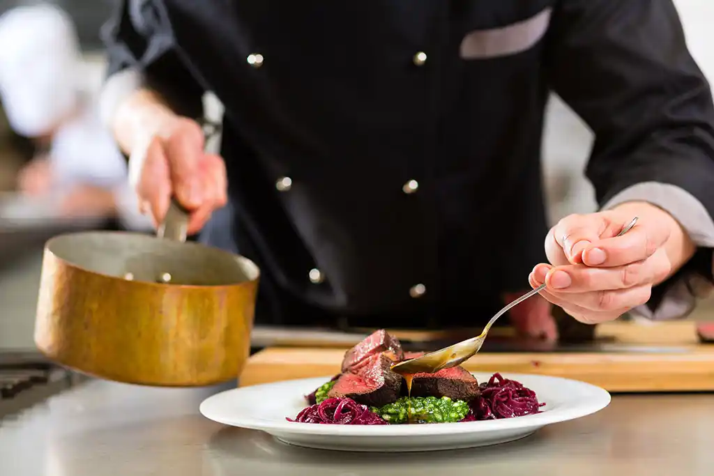 Chefkoch Richard Dafner beim Anrichten von rosa gebratenem Rinderhüftsteak mit Gemüse.